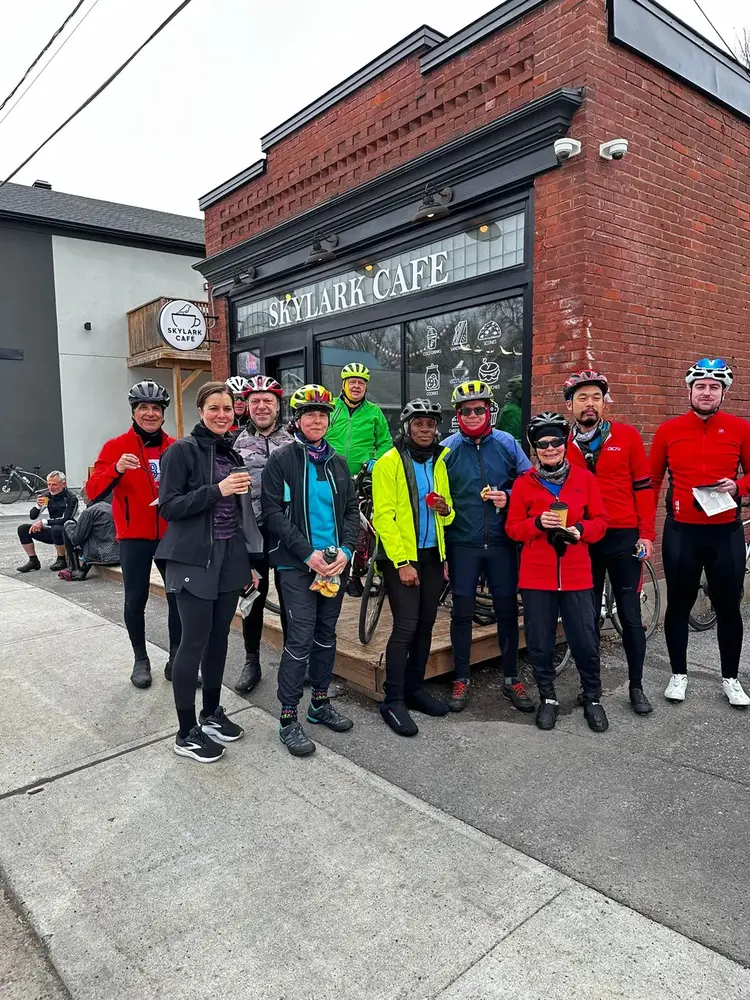 A cycling group posing with coffee in front of Skylark Café
